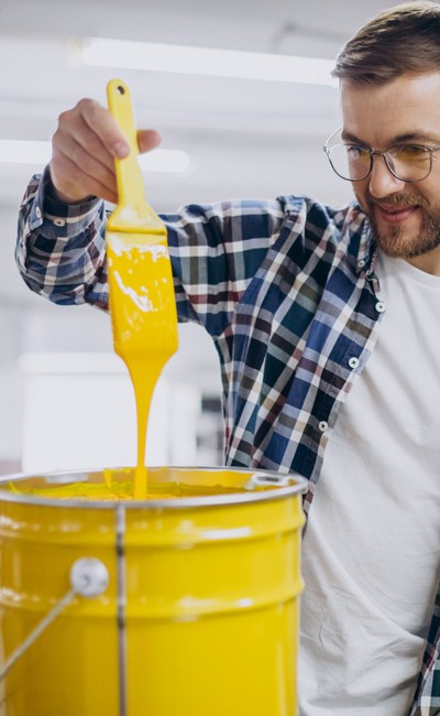 a man holding pain brush filled with yellow pain over paint container