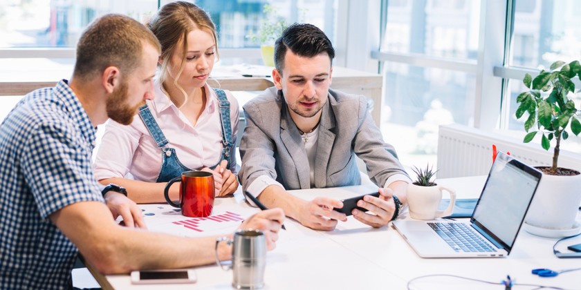 3 people looking at a laptop in an office